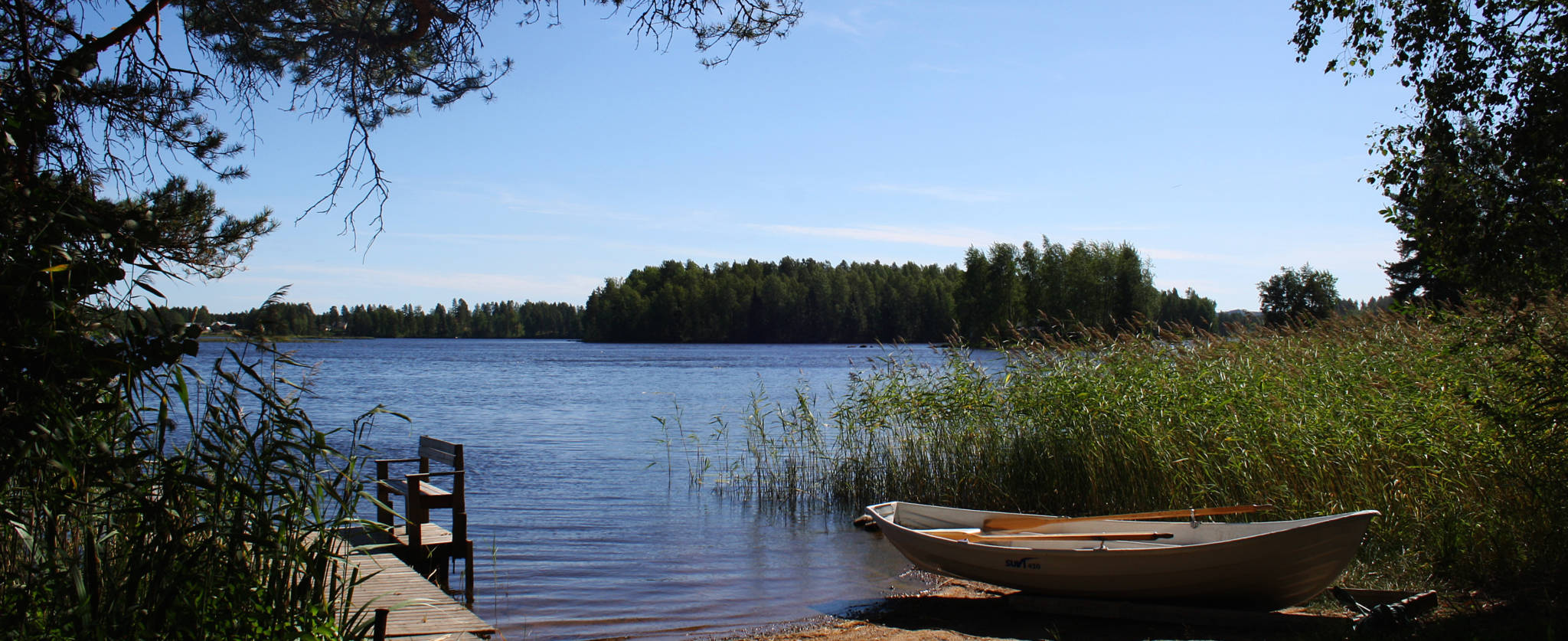 järvi, kaislikko, laituri ja vene kesäpäivänä