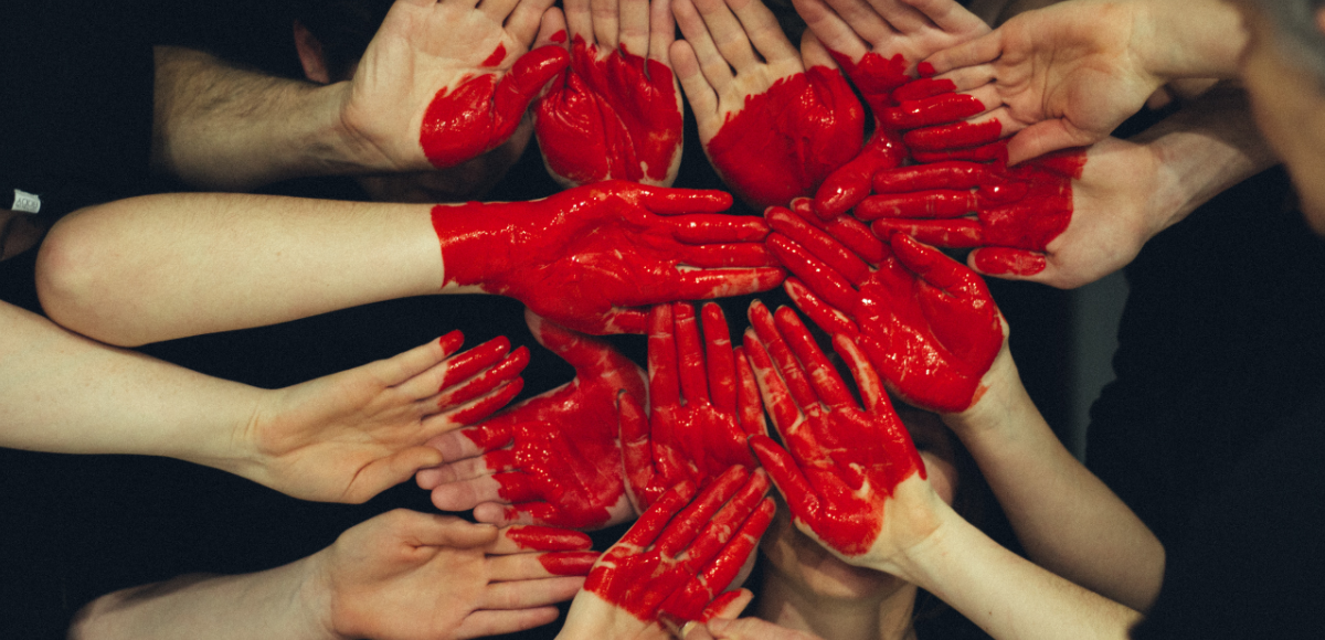 käsiä, joista osa maalattu punaiseksi siten, että syntyy sydämen-kuva